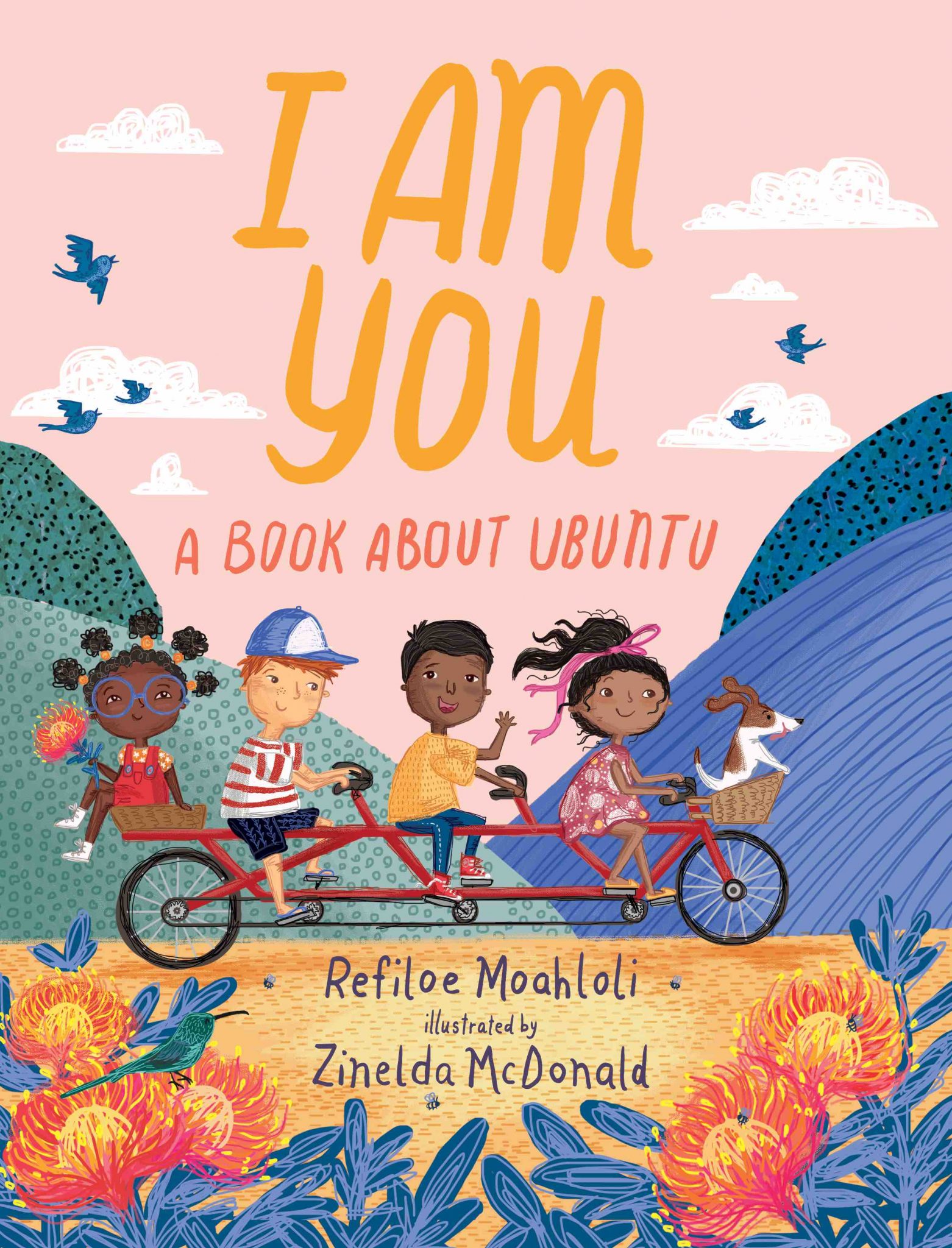 Cover for I am You: A Book about Ubuntu featuring an illustration of four kids who are all of different ethnicities on a tandem bicycle that seats three with a dog in the front basket and the last kid in the back basket. They're riding through a colorful natural landscape of rolling hills where each hill is a different color and orange flowers are in the foreground. The ground is orange and the sky is light pink with blue birds in it. The title is displayed in orange and pink.